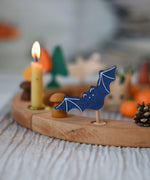 A Grimm's wooden bat decorative figure placed on a natural Grimm's celebration ring. A lit candle and other decorative items can be seen placed on the ring in the background. 
The decorative figures are part of a wide range of figures and rings available here at Babipur.