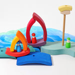 A small world play scene set up using the pieces from the Grimm's Stacking Tower Boat Set, some Grimm's friends peg dolls and blue material. 