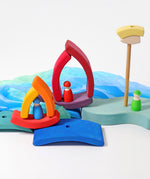 A small world play scene set up using the pieces from the Grimm's Stacking Tower Boat Set, some Grimm's friends peg dolls and blue material. 