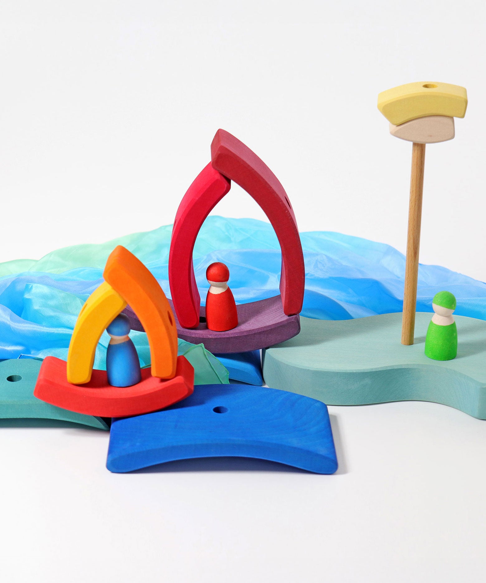 A small world play scene set up using the pieces from the Grimm's Stacking Tower Boat Set, some Grimm's friends peg dolls and blue material. 