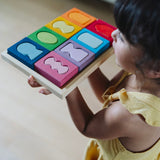 A child holding the Grimm's windows building set blocks set on the floor in front of them. These Grimm's toys are part of a wide range of wooden toys available here at Babipur. 