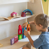 A child playing with the Grimm's Windows Building & Stacking Set. The child is stacking them on top of each other and using the shapes as decorations. These Grimm's toys are part of a wide range of wooden toys available here at Babipur. 