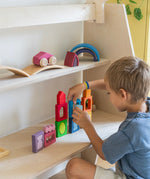 A child playing with the Grimm's Windows Building & Stacking Set. The child is stacking them on top of each other and using the shapes as decorations. These Grimm's toys are part of a wide range of wooden toys available here at Babipur. 