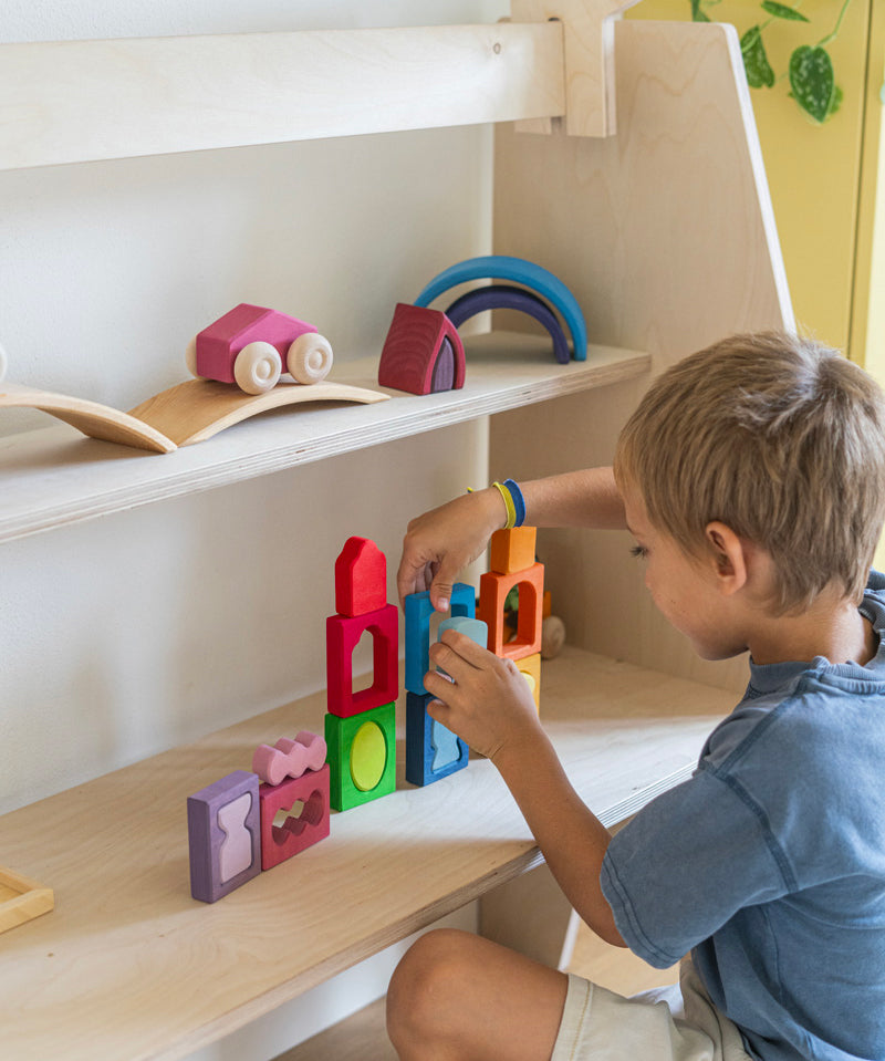 A child playing with the Grimm's Windows Building & Stacking Set. The child is stacking them on top of each other and using the shapes as decorations. These Grimm's toys are part of a wide range of wooden toys available here at Babipur. 