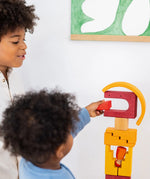 Child holding a wooden block from the Grimms desert sand building set on a tower showing scale