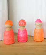 A set of 3 Grimms wooden neon pink friend peg dolls standing on a wooden surface