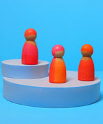 A set of three Grimms wooden neon pink friend peg dolls standing on a blue platform.