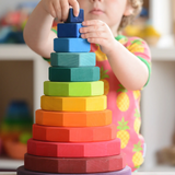 Child placing a block on Grimms large handcrafted wooden geometric stacker in a rainbow palette