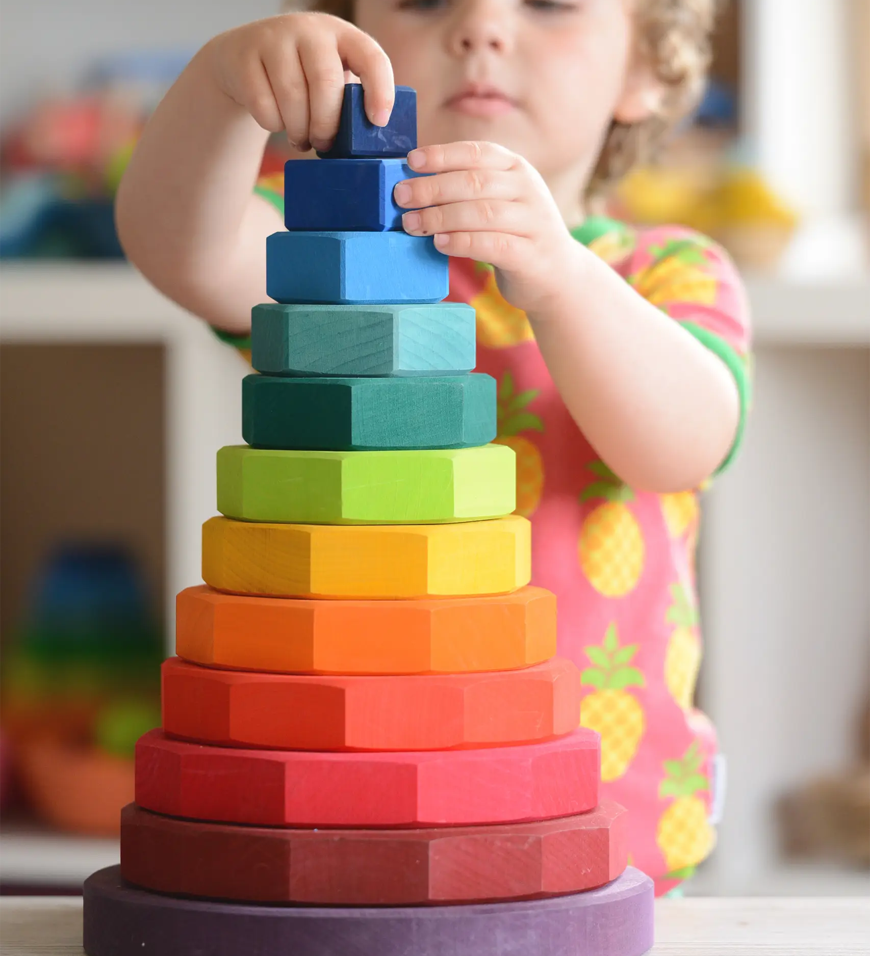 Child placing a block on Grimms large handcrafted wooden geometric stacker in a rainbow palette