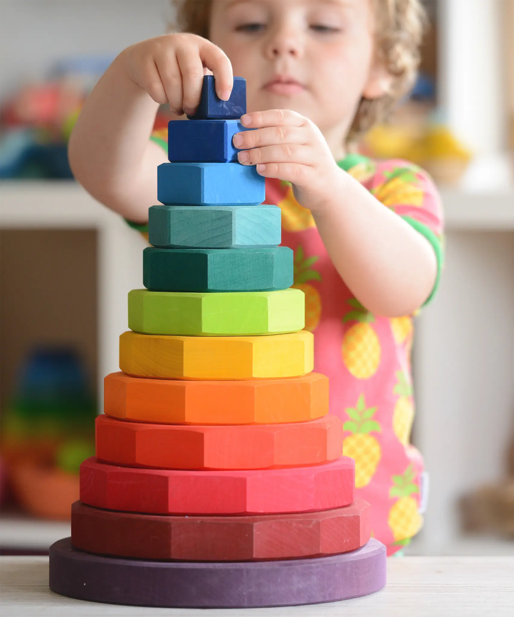 Child placing a block on Grimms large handcrafted wooden geometric stacker in a rainbow palette