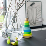 Grimms handcrafted wooden neon green peg dolls on a table next to a large matching stacking tower