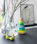 Grimms handcrafted wooden neon green peg dolls on a table next to a large matching stacking tower