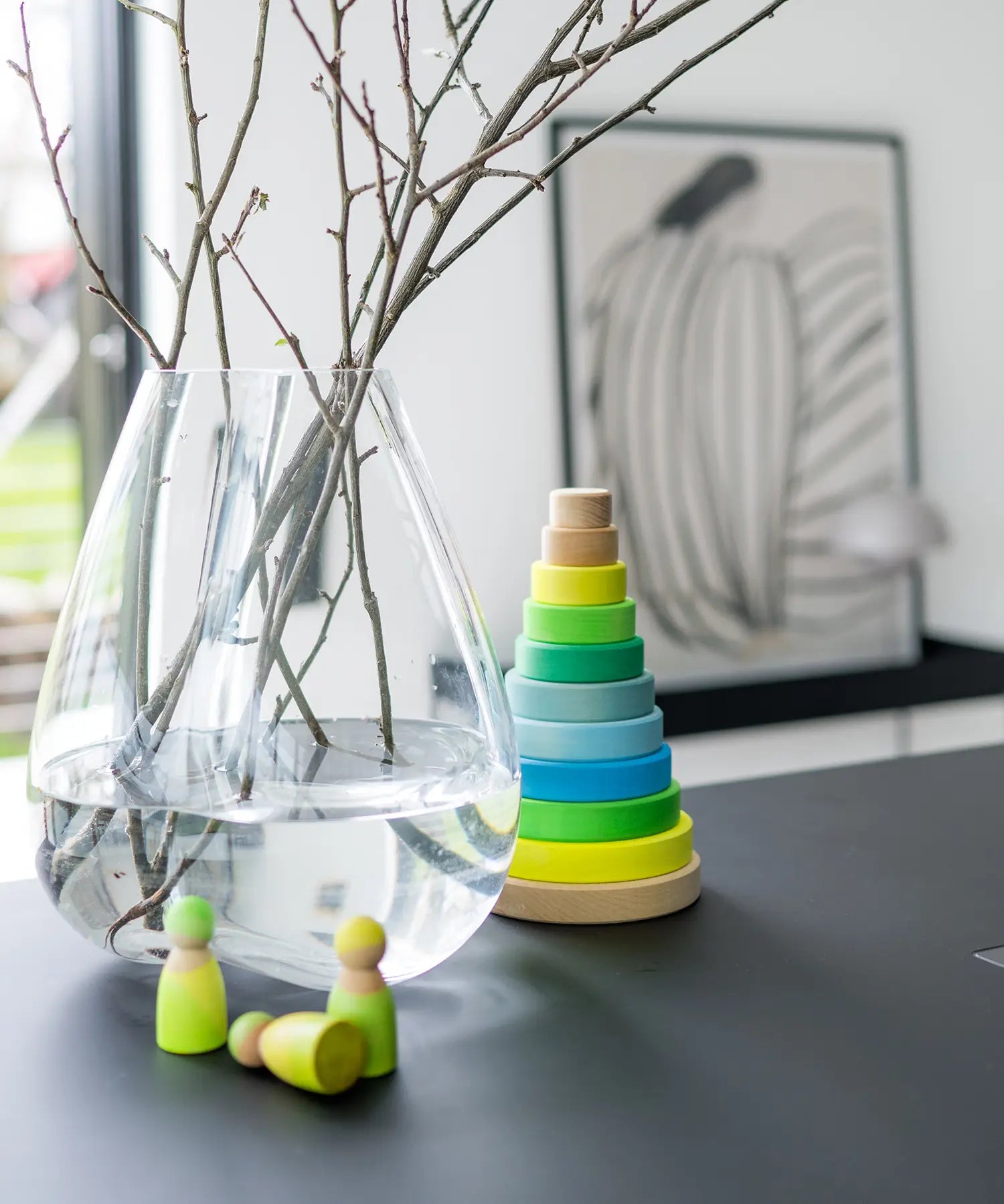 Grimms handcrafted wooden neon green peg dolls on a table next to a large matching stacking tower