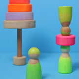 Grimms handcrafted wooden neon green peg dolls balancing on a neon pink wooden stacking disk
