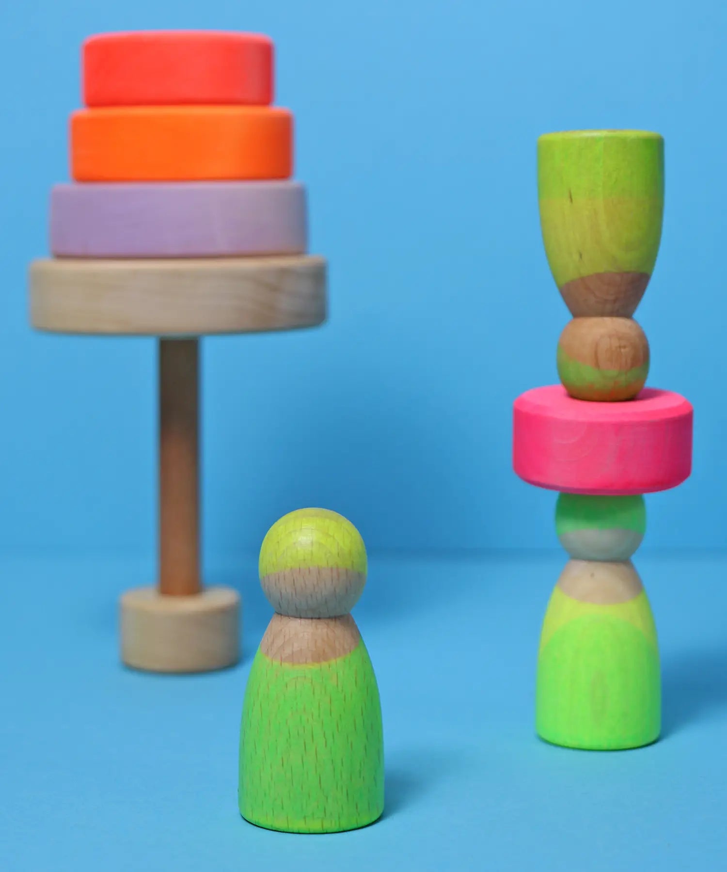 Grimms handcrafted wooden neon green peg dolls balancing on a neon pink wooden stacking disk