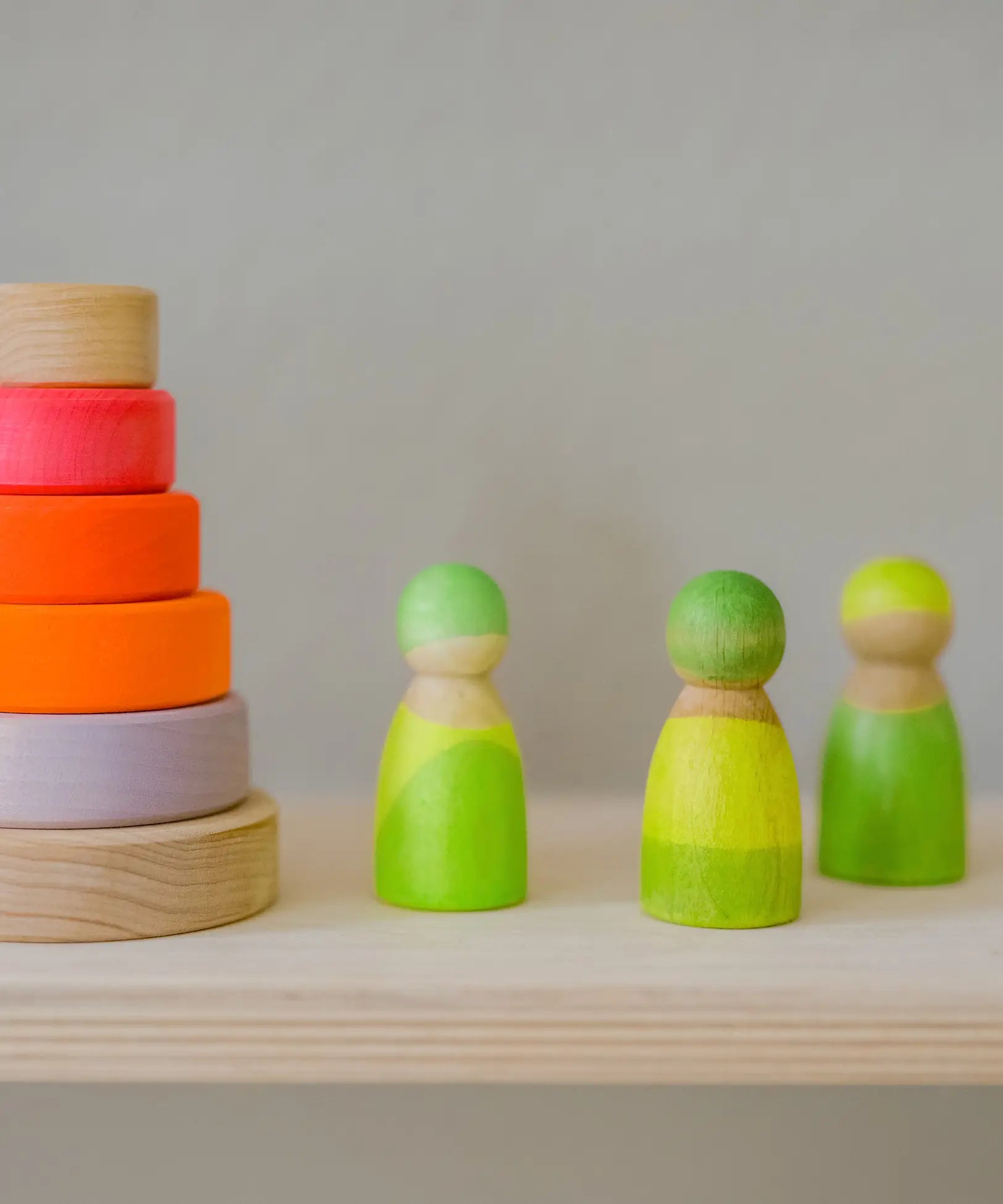 Grimms handcrafted wooden neon green peg dolls next to a small neon pink stacking tower