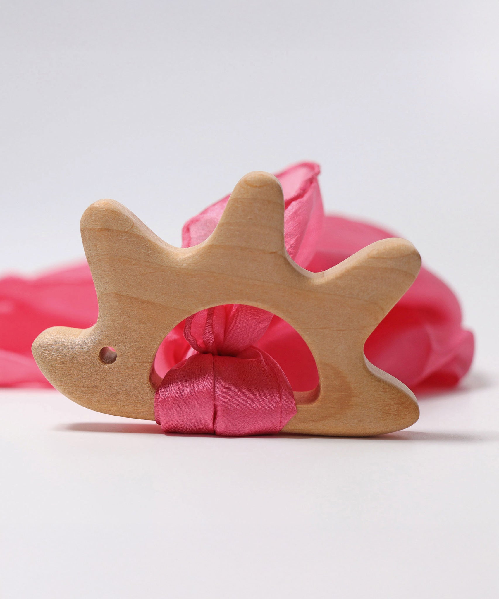 A Grimm's Hedgehog shaped wooden grasping toy with a piece of pink ribbon material attached. 
