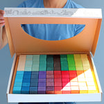 A person holding open a box that contains a Grimm's Large Mosaic Square set. 