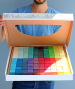 A person holding open a box that contains a Grimm's Large Mosaic Square set. 
