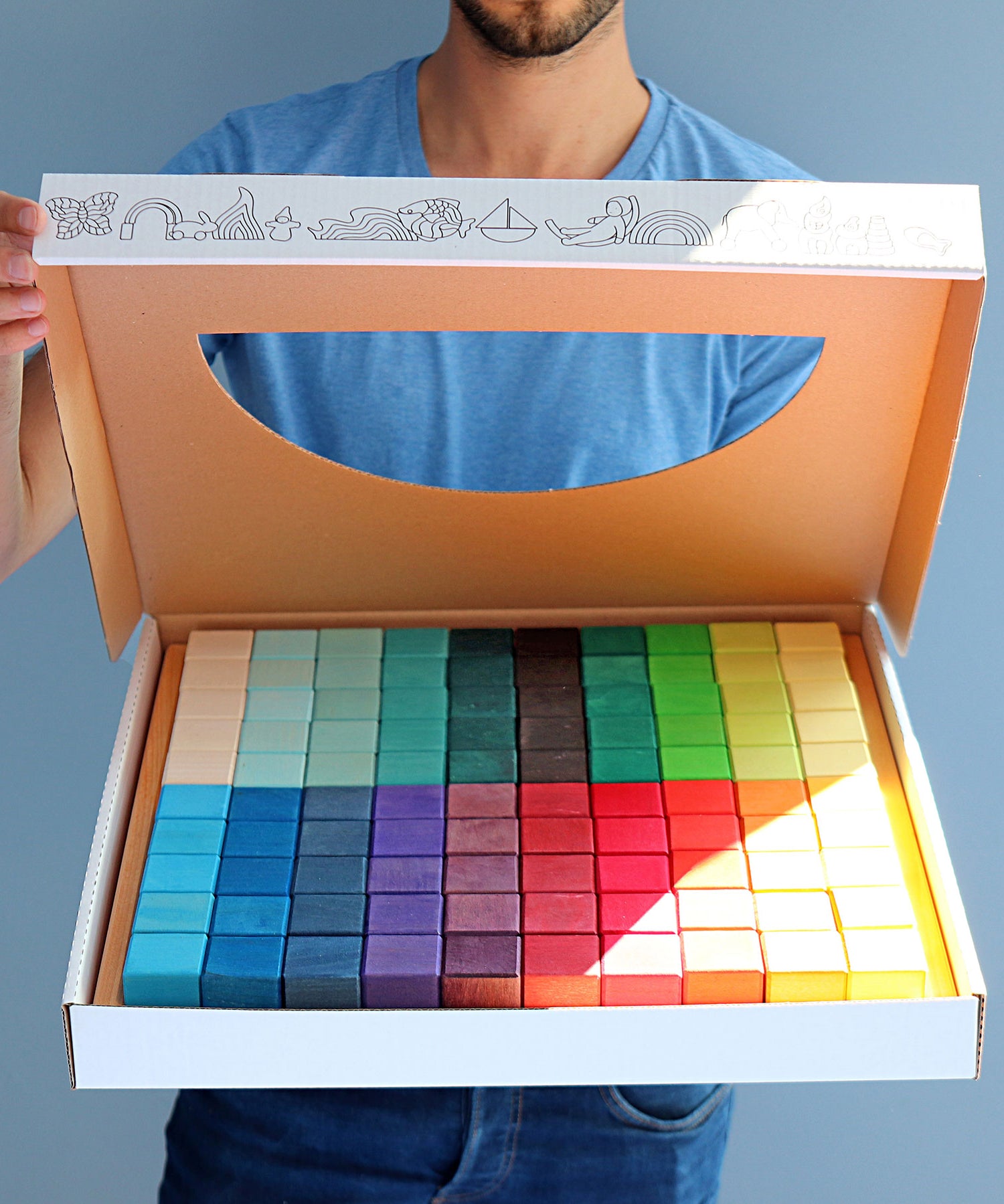 A person holding open a box that contains a Grimm's Large Mosaic Square set. 