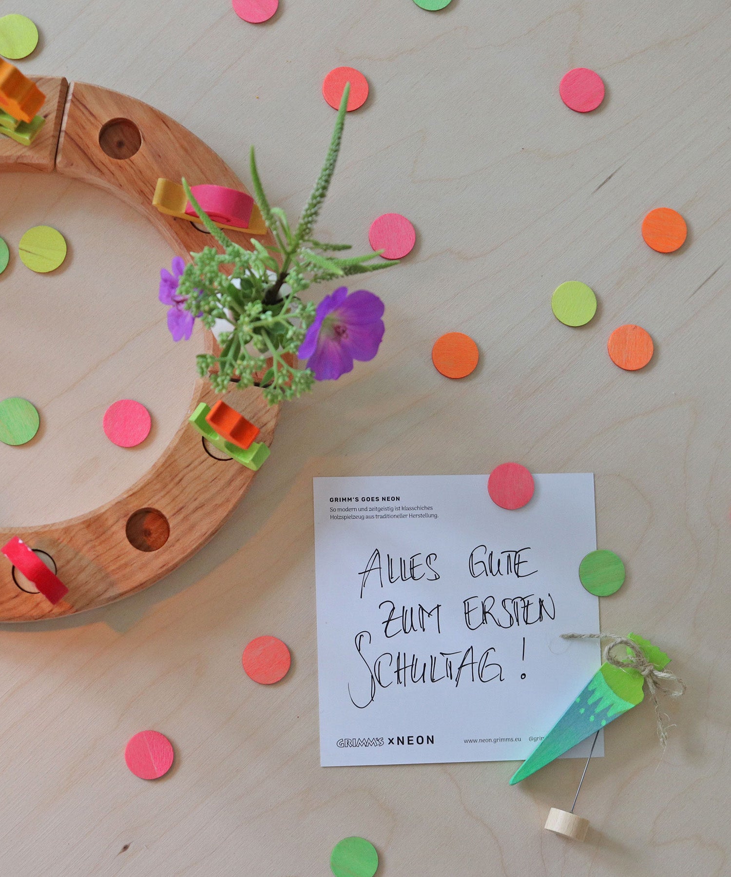 A flatlay of the green and pink neon birthday cone decorative figures next to the mixed neon confetti dots  and a celebration ring on a wooden surface 