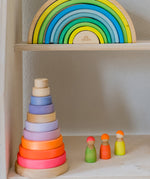 Grimms wooden neon green rainbow on a shelf above a neon pink conical tower next to 3 mixed wooden friends.