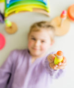 A child lying down holding the yellow and orange neon coloured Grimms wooden friend showing the scale
