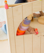 A close up view of a child playing with a neon pink Grimms wooden friend showing the scale with pieces of the large conical tower stacked on top of eachother