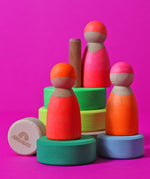 A set of 3 Grimms neon pink wooden friend dolls standing on the pieces from the small green conical tower