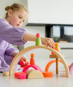 A child playing with the neon pink wooden conical tower and rainbow with the mixed neon friends on top