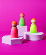 Grimms wooden friends in a hand painted neon mix finish standing on 2 wooden pink platforms