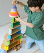 A child stacking the Grimms blue neon wooden rainbow with a conical tower on top. 
