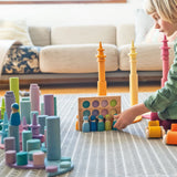 Child playing with Grimms peg dolls in a creative play scene including pastel coins, forest and roller sets