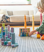 Child playing with Grimms peg dolls in a creative play scene including pastel coins, forest and roller sets