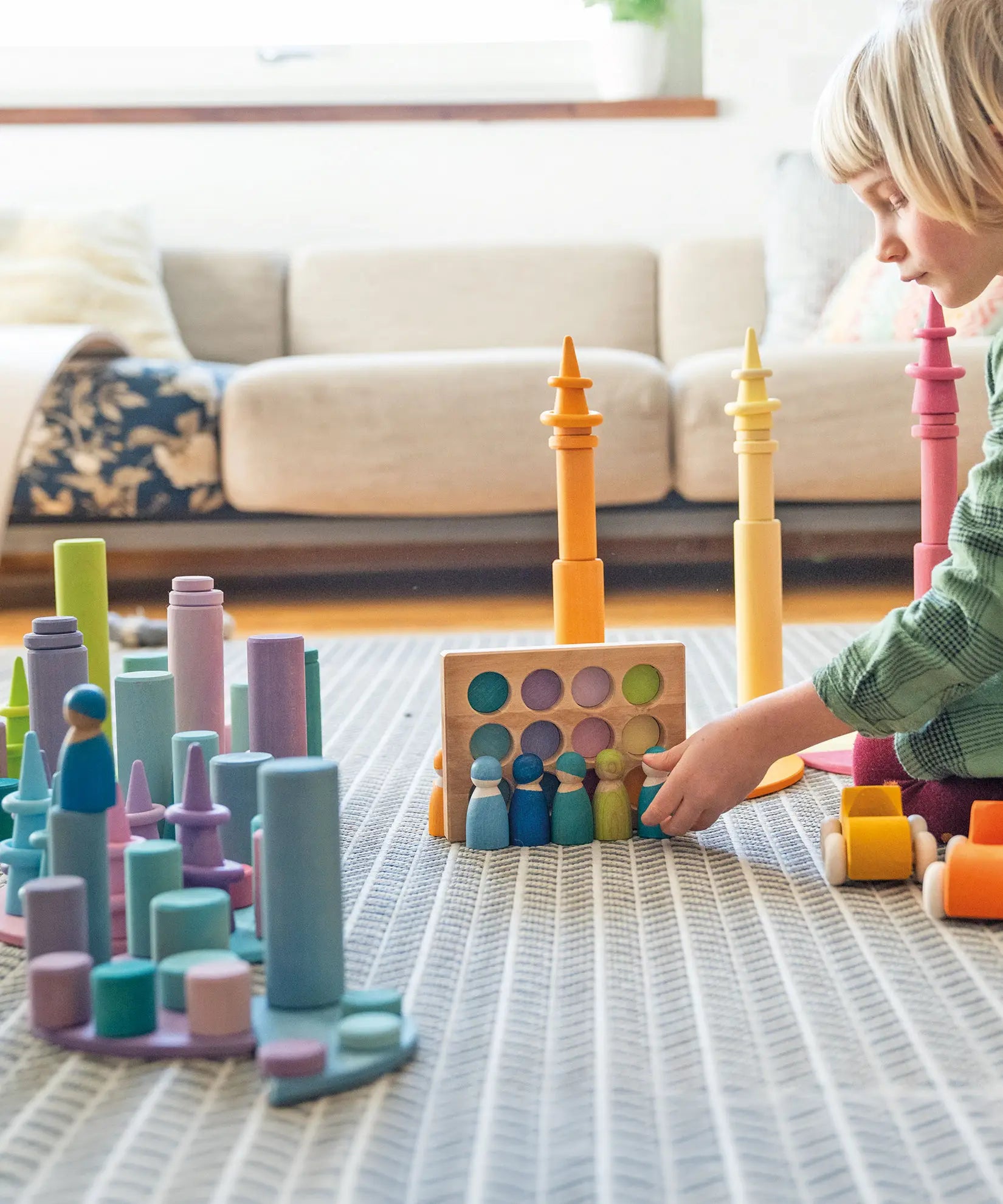 Child playing with Grimms peg dolls in a creative play scene including pastel coins, forest and roller sets