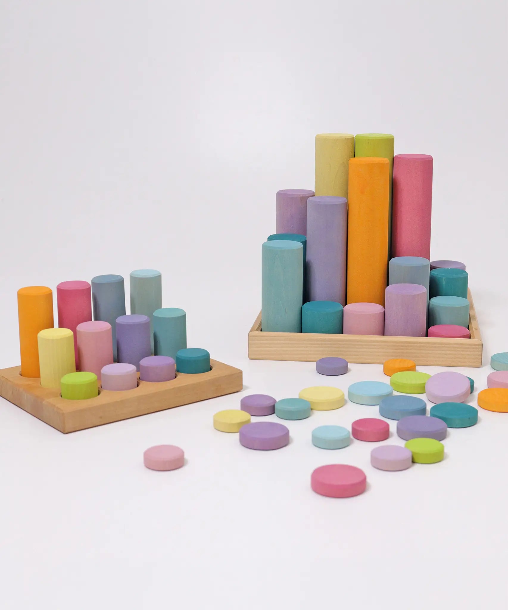 Loose Grimms wooden coins next to cylinder roller stacking sets all in a pastel palette