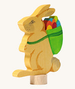 A close up of the Grimms wooden rabbit decorative figure holding a green basket full of multicoloured eggs. Showing the hand painted finish detail 