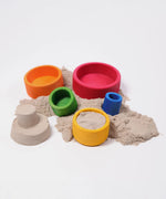 Grimms bright rainbow wooden sorting bowls with sand inside next to a small sandcastle