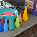 Toddler holding on a Grimms wooden forest piece on a wall. Showing other coloured wooden cone pieces