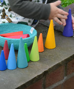 Toddler holding on a Grimms wooden forest piece on a wall. Showing other coloured wooden cone pieces