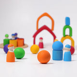 Loose Grimms handcrafted wooden house pieces in a rainbow palette made into a structure with matching peg dolls and balls in front.