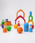 Loose Grimms handcrafted wooden house pieces in a rainbow palette made into a structure with matching peg dolls and balls in front.