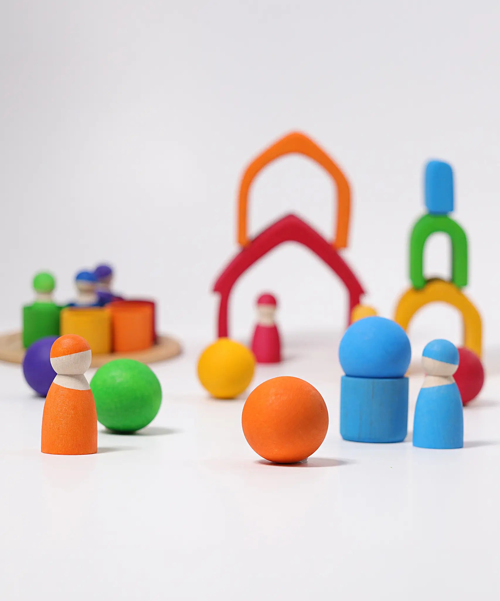 Loose Grimms handcrafted wooden house pieces in a rainbow palette made into a structure with matching peg dolls and balls in front.