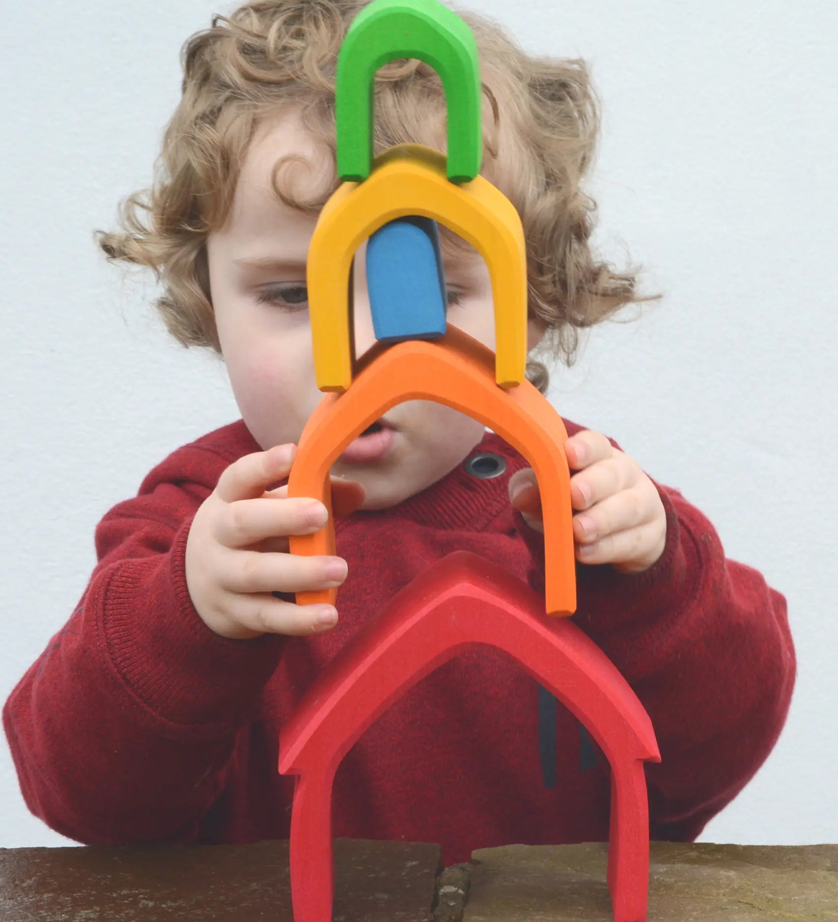 Child stacking the Grimm's house shaped pieces in a rainbow palette