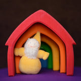 Grimm's handcrafted wooden house in a rainbow palette with a small yellow bearded dwarf doll standing underneath