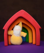 Grimm's handcrafted wooden house in a rainbow palette with a small yellow bearded dwarf doll standing underneath