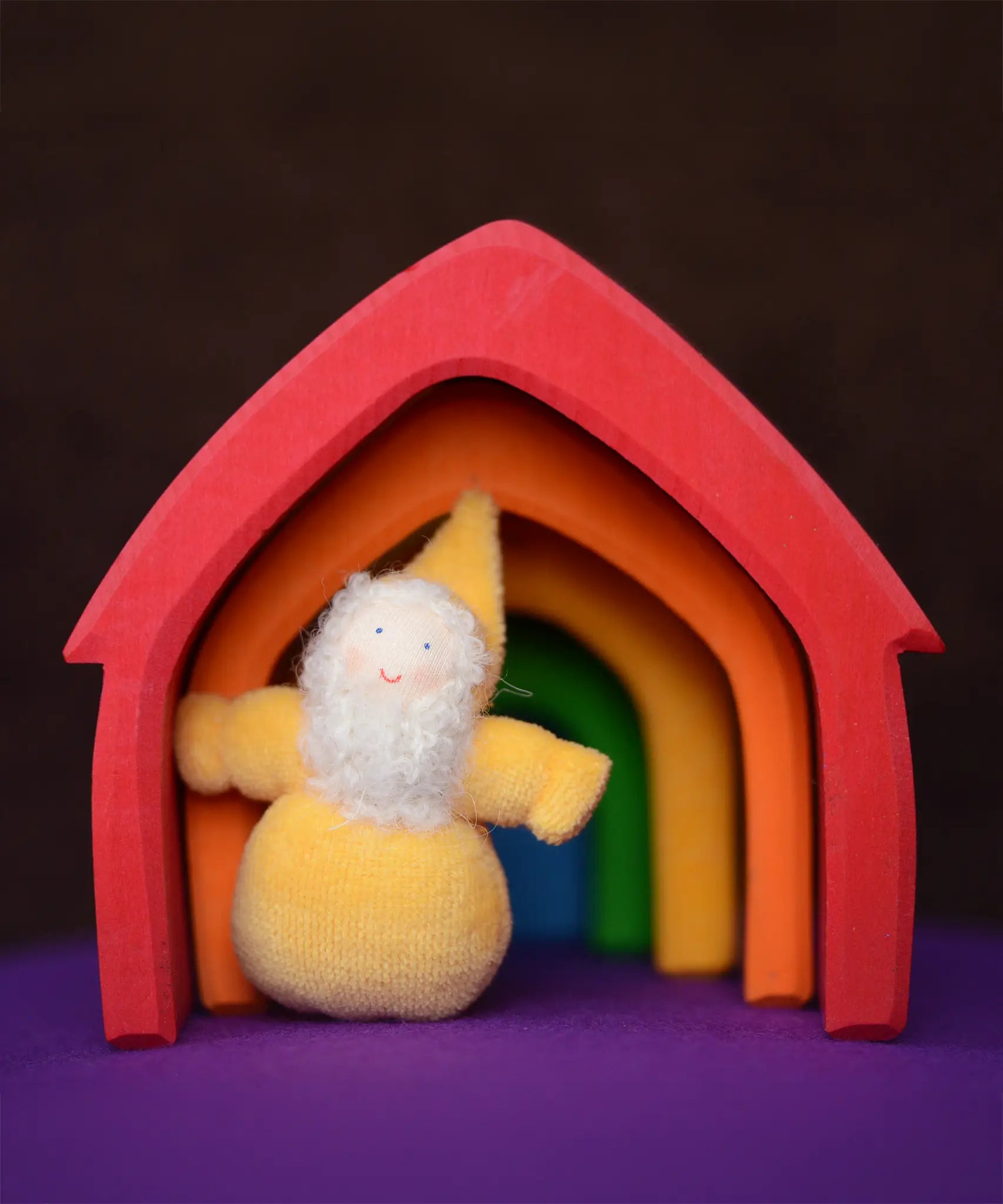 Grimm's handcrafted wooden house in a rainbow palette with a small yellow bearded dwarf doll standing underneath