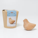 The Grimm's wooden relaxing bird toy shown next to it's plastic free, cardboard packaging box.