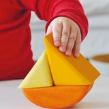 Child holding a Grimms wooden triangular shape from the rolling boats set showing scale