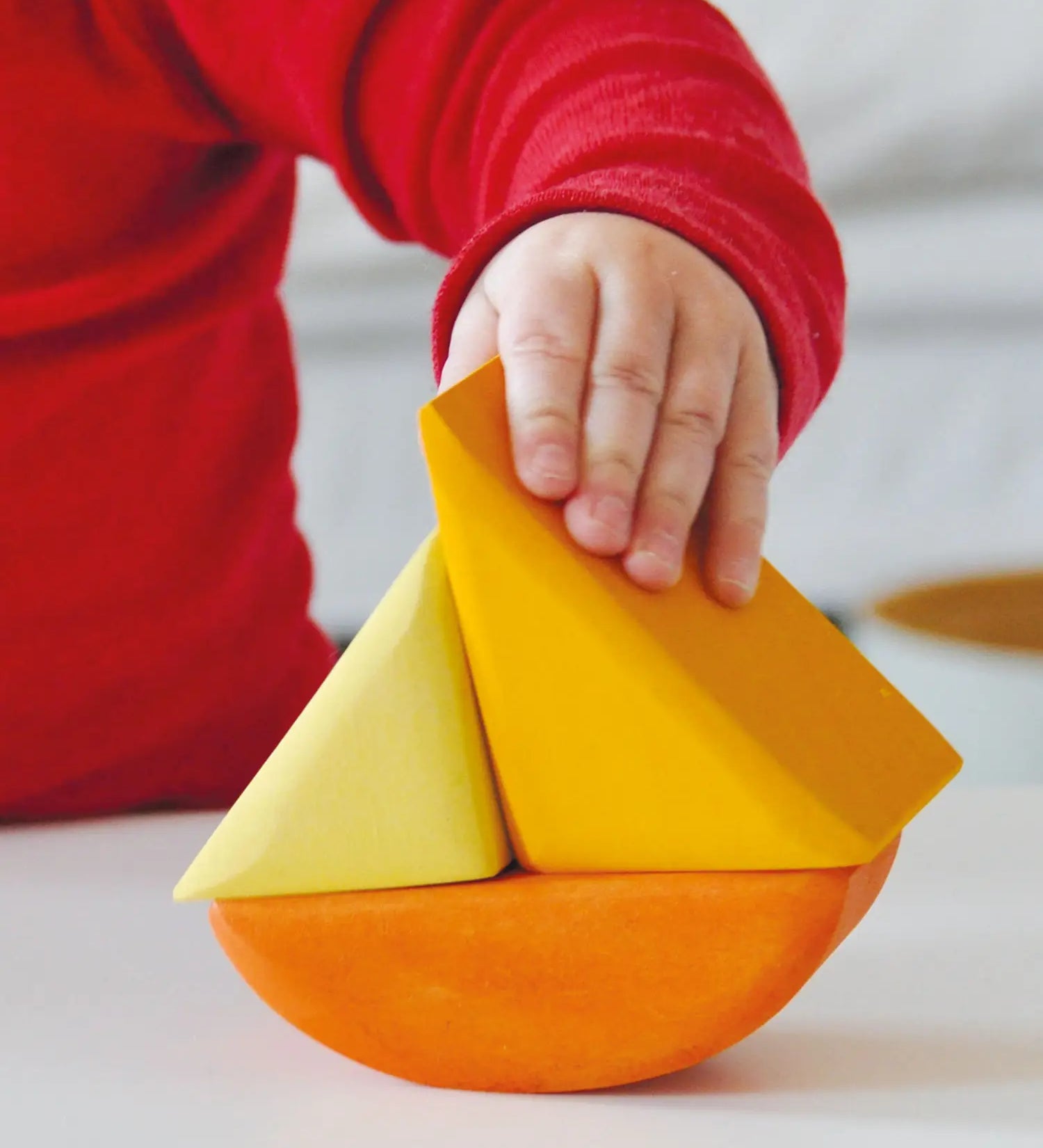 Child holding a Grimms wooden triangular shape from the rolling boats set showing scale